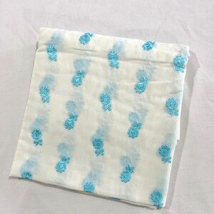 May include: White fabric with a light blue floral pattern. The fabric is folded in half and has a soft, textured feel.