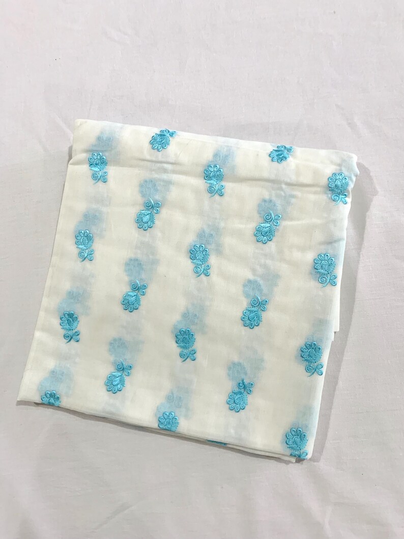 May include: White fabric with a light blue floral pattern. The fabric is folded in half and has a soft, textured feel.