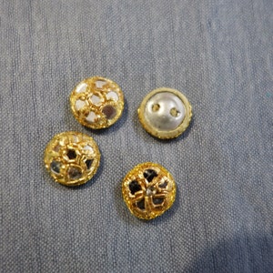 May include: Four decorative buttons with gold trim. Two buttons have a mirrored surface with a geometric design. One button has a white surface with two holes. One button has a black surface with a geometric design.