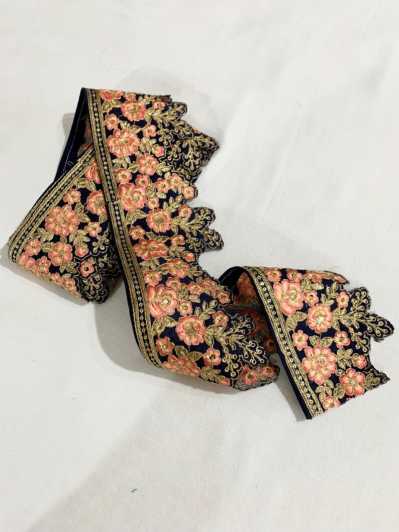 May include: A navy blue lace trim with pink and gold floral embroidery. The trim has a scalloped edge and is perfect for adding a touch of elegance to any project.