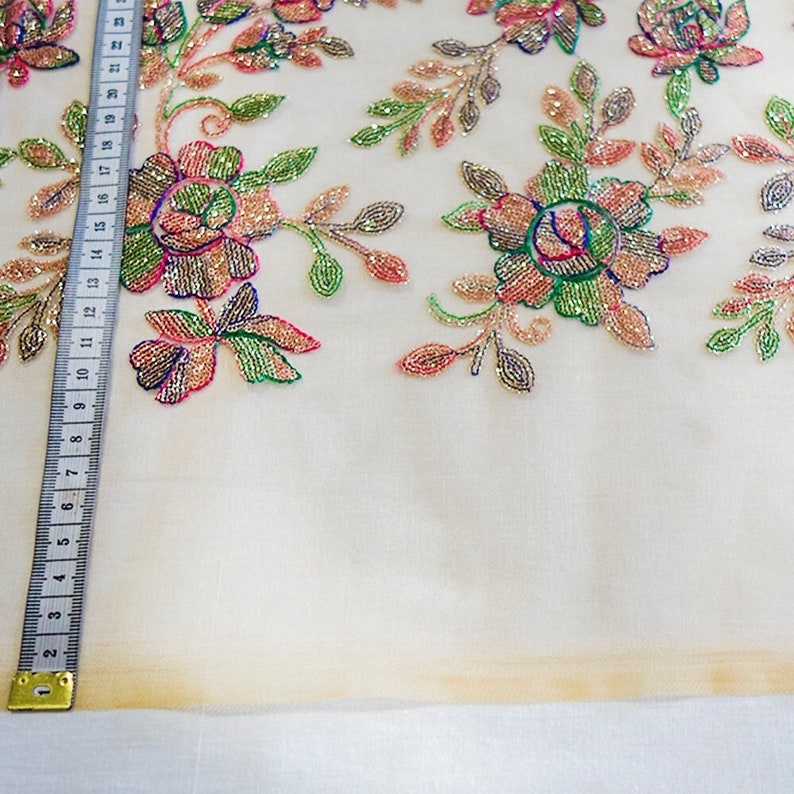 May include: White sheer fabric with a floral design embroidered with iridescent beads. The fabric is decorated with pink, green, and gold beads.
