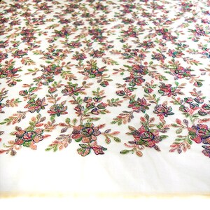May include: White fabric with a floral pattern embroidered with iridescent sequins. The flowers are pink, green, and blue.