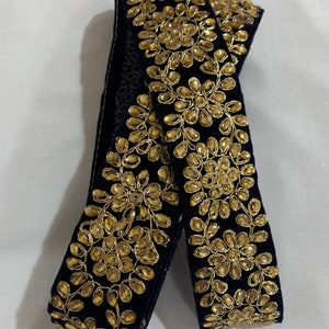 May include: Black velvet trim with gold embroidery and embellishments. The trim features a repeating pattern of floral designs.