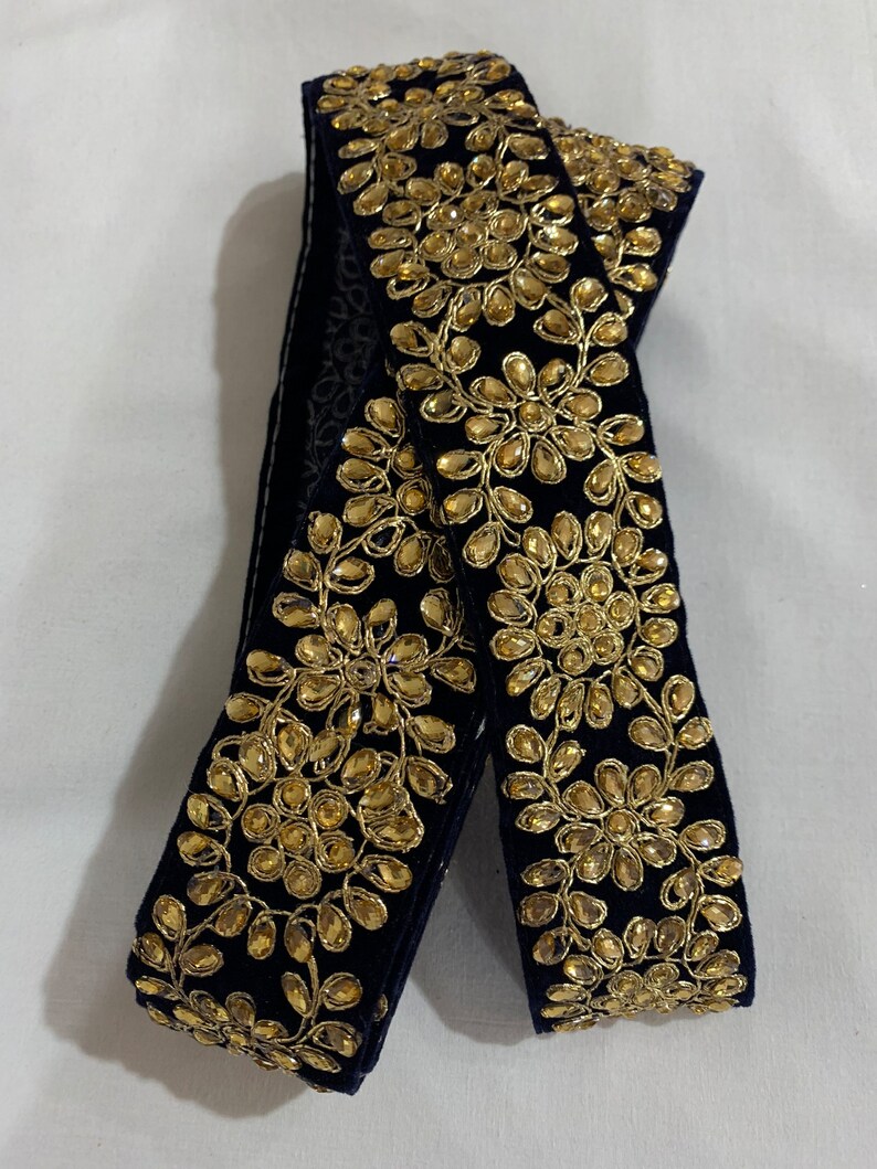 May include: Black velvet trim with gold embroidery and embellishments. The trim features a repeating pattern of floral designs.