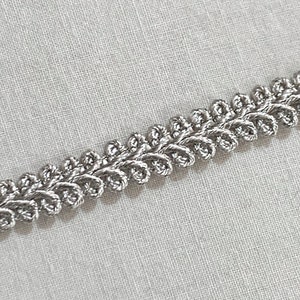 Puede incluir: Borde trenzado plateado con un diseño decorativo de bucle. Esta cinta es perfecta para agregar un toque de elegancia a cualquier proyecto.