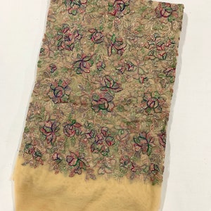 May include: Beige sheer fabric with a floral pattern embroidered with silver, green, pink, and blue thread. The fabric has a subtle shimmer.