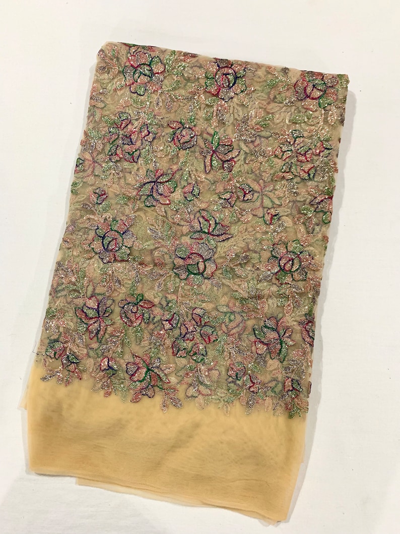 May include: Beige sheer fabric with a floral pattern embroidered with silver, green, pink, and blue thread. The fabric has a subtle shimmer.