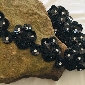 May include: Black beaded trim with sequined flower embellishments. The trim features clusters of black flowers with clear rhinestone centers.