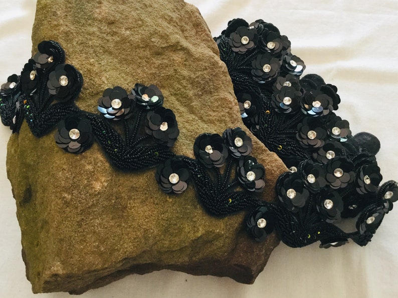 May include: Black beaded trim with sequined flower embellishments. The trim features clusters of black flowers with clear rhinestone centers.