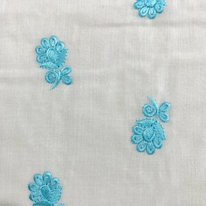 May include: White fabric with a repeating pattern of blue embroidered flowers.
