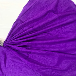 May include: A purple fabric with a textured surface. The fabric is folded and draped over a white surface.