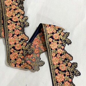 May include: A navy blue lace trim with gold and pink floral embroidery. The trim has a scalloped edge and is perfect for adding a touch of elegance to any project.