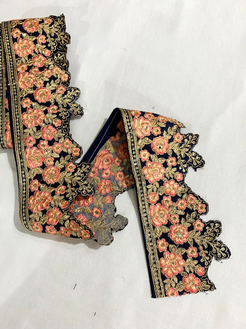 May include: A navy blue lace trim with gold and pink floral embroidery. The trim has a scalloped edge and is perfect for adding a touch of elegance to any project.