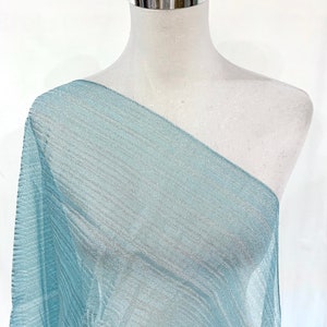 Puede incluir: Una tela transparente de color azul claro con un brillo sutil. La tela está drapeada sobre un maniquí blanco.