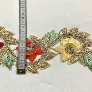 May include: Gold, orange, and green beaded trim with floral designs and rhinestones. The trim is approximately 7 inches long.