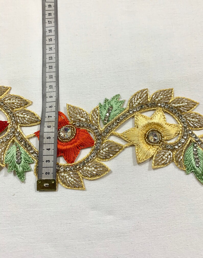 May include: Gold, orange, and green beaded trim with floral designs and rhinestones. The trim is approximately 7 inches long.