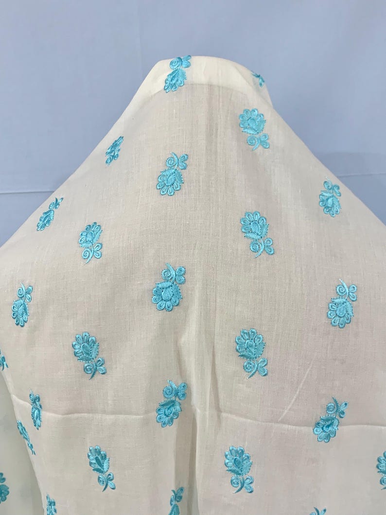 May include: White fabric with a light blue floral embroidery pattern.