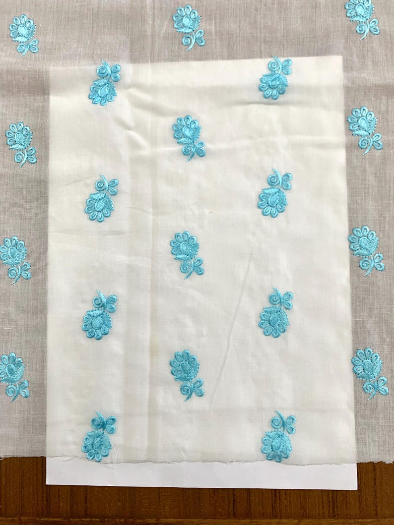 May include: White fabric with a light blue floral embroidery pattern. The fabric is folded in half and the embroidery is visible on both sides.