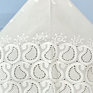 May include: White cotton fabric with a delicate, embroidered paisley pattern. The fabric has a scalloped edge and is perfect for crafting projects.