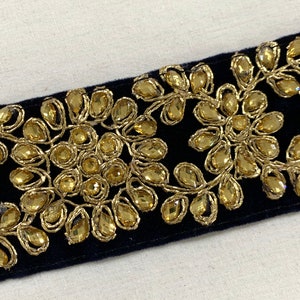 May include: Black velvet trim with gold embroidery and clear rhinestones. The trim features a floral design.