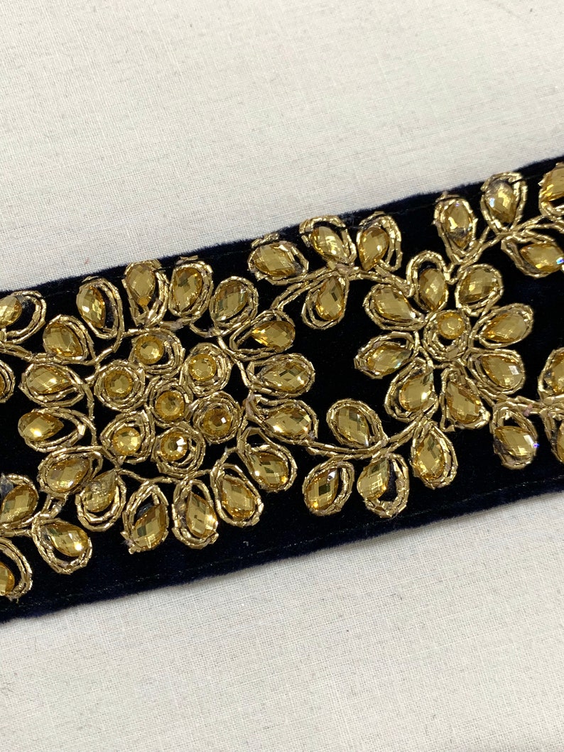 May include: Black velvet trim with gold embroidery and clear rhinestones. The trim features a floral design.