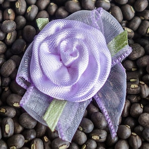 Puede incluir: Una rosa de satén lavanda con una superposición de tul con volantes. La rosa está sobre un fondo de frijoles negros.