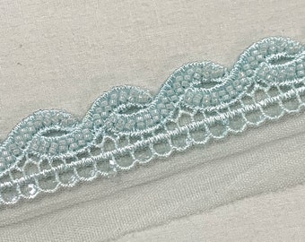 Pode incluir: Bordado de renda azul claro com uma borda festonada. A renda é delicada e tem um brilho sutil.
