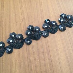 May include: Black beaded trim with a repeating pattern of floral designs. Each flower is made of black sequins with a clear rhinestone center.