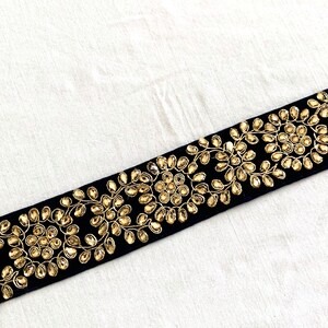 May include: Black velvet trim with gold embroidery and rhinestones. The trim features a repeating pattern of floral designs with circular embellishments.