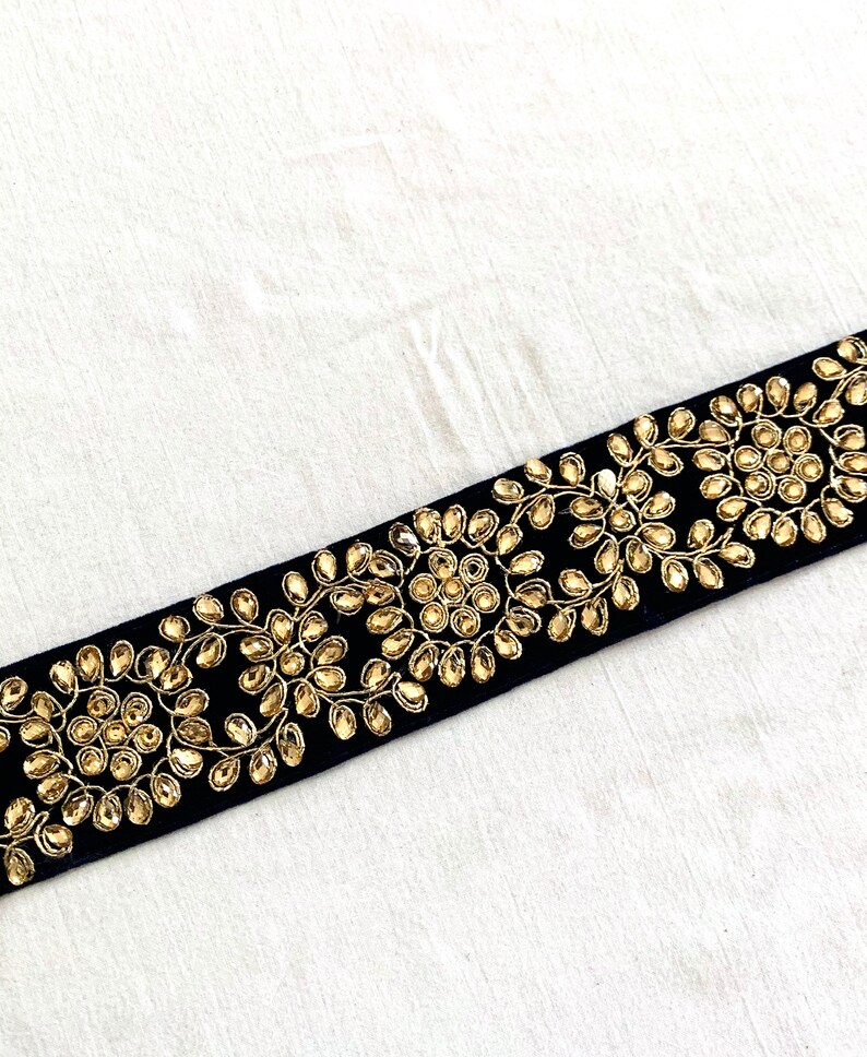 May include: Black velvet trim with gold embroidery and rhinestones. The trim features a repeating pattern of floral designs with circular embellishments.
