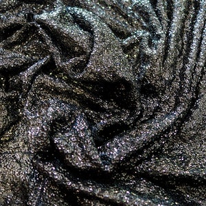 Könnte beinhalten: Nahaufnahme eines schwarzen Stoffes mit einem glitzernden, schillernden Finish. Der Stoff besteht aus Pailletten und hat eine knitterige Textur.