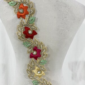 May include: Gold trim lace with red, orange, and pink flowers and clear rhinestones.