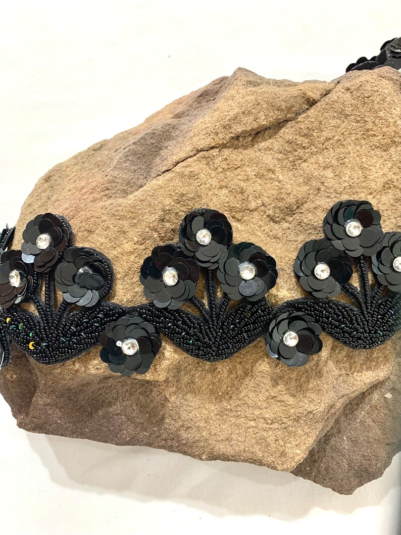 May include: Black beaded trim with black flower embellishments and clear rhinestones.