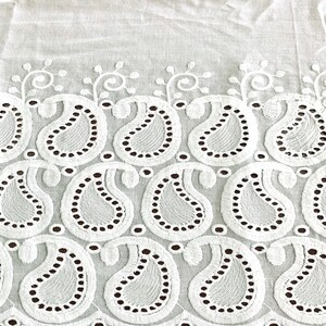 May include: White cotton fabric with a delicate embroidered border featuring a paisley pattern. The border has a scalloped edge with small circles.
