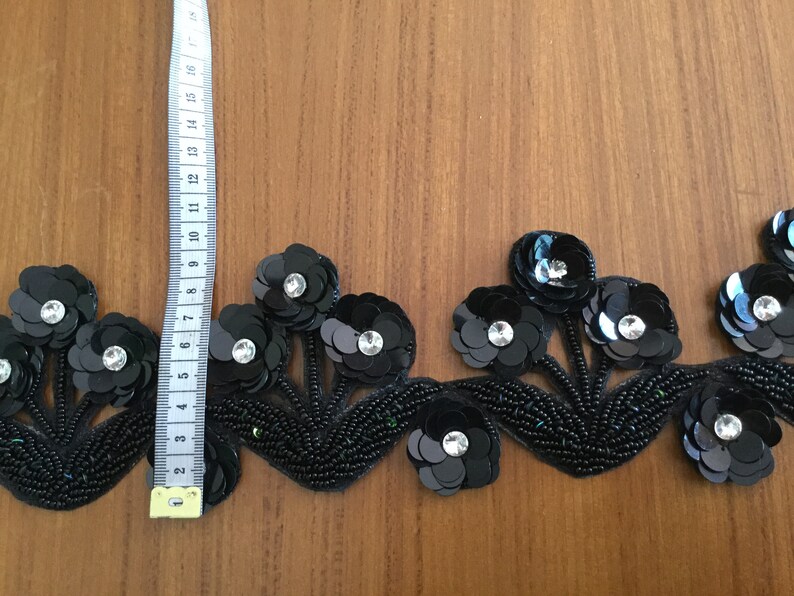 May include: Black beaded trim with black and silver sequins in a floral design. The trim is approximately 3 inches wide.