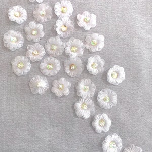 May include: A cluster of white fabric flowers with iridescent centers arranged in a cascading pattern on a light gray background.