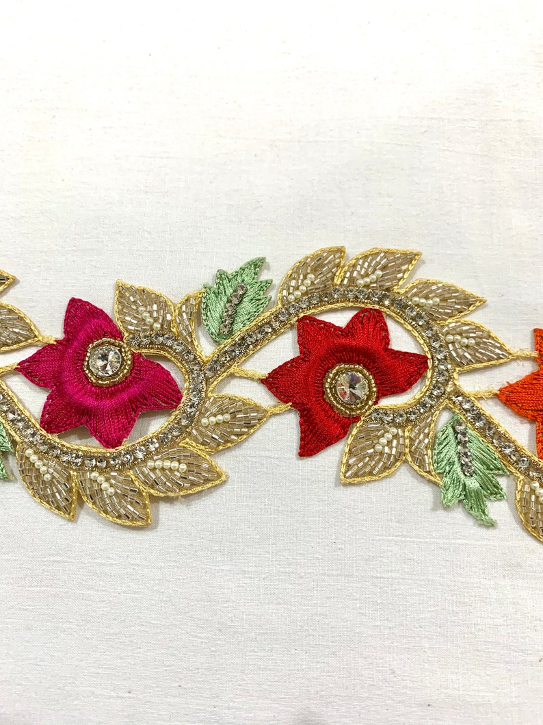May include: Gold embroidered trim with red, orange, and green floral designs. The trim features small pearl-like beads and rhinestones.