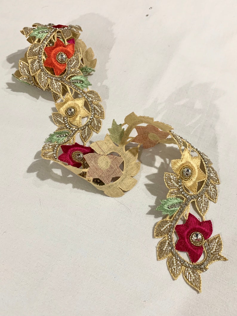 May include: Gold trim lace with floral embroidery and beaded accents. The lace features red, orange, and green flowers with clear rhinestones in the center.