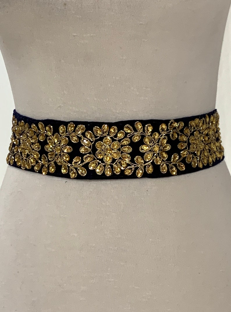May include: A black velvet belt with gold floral embroidery. The belt is adorned with small, round, gold-colored embellishments.