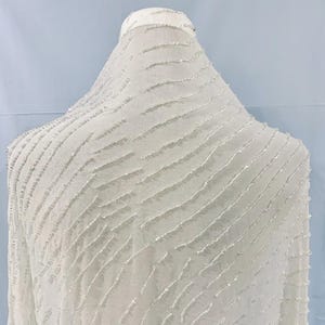May include: White beaded fabric with a wavy pattern. The fabric is sheer and has a delicate texture.