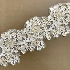 May include: White lace trim featuring a floral design and silver rhinestones. The trim is delicate and intricate, ideal for adding a touch of elegance to any project.