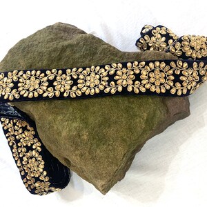 May include: Black velvet trim with gold embellishments. The trim features a repeating pattern of small, round, gold beads arranged in a circular design.