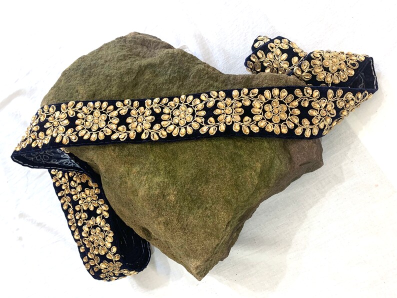 May include: Black velvet trim with gold embellishments. The trim features a repeating pattern of small, round, gold beads arranged in a circular design.