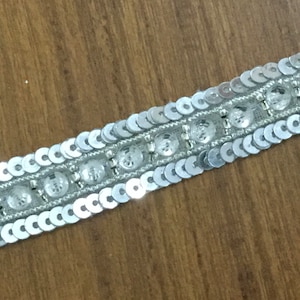 Puede incluir: Adorno plateado con lentejuelas y cuentas transparentes. El adorno tiene aproximadamente 2,5 cm de ancho.
