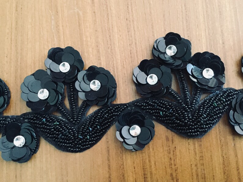May include: Black beaded trim with black sequin flowers and clear rhinestones. The trim is perfect for adding a touch of elegance to any project.