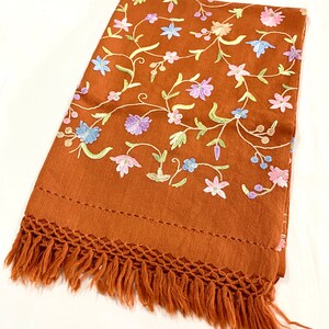 May include: A brown shawl with a floral embroidery pattern. The shawl has a fringe border.