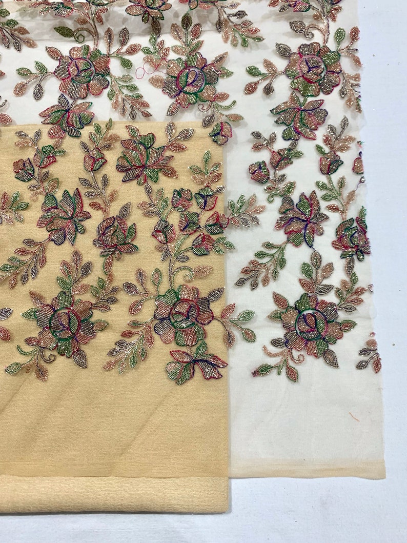 May include: Beige and white fabric with floral embroidery. The embroidery features small, colorful beads and sequins in shades of pink, green, and gold. The fabric is sheer and delicate.