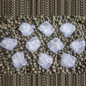 Peut inclure: Dix décorations blanches en dentelle en forme de fleur sont disposées sur un lit de haricots bruns.