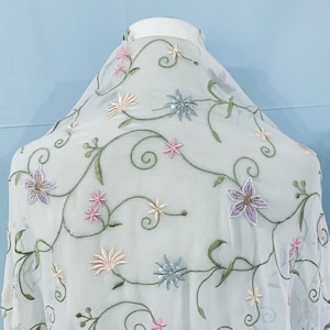 May include: White sheer fabric with embroidered floral vines in shades of green, pink, and blue. The flowers are scattered throughout the fabric and have a delicate, feminine look.