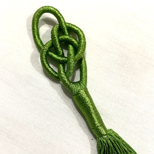Op de afbeelding: Een groene kwast met een geknoopte bovenkant. De knoop is een complex ontwerp met meerdere lussen.